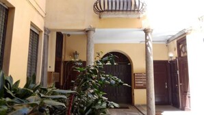 Une entrée d’immeuble avec une porte en bois, un balcon doté de rampes en métal et une colonne.