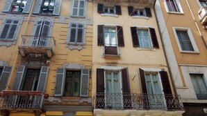 A multi-story building with balconies, windows with shutters, and a visible door.