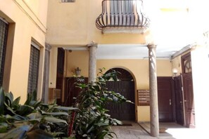 Una entrada de edificio con puerta de madera, un balcón con barandilla metálica y una columna.