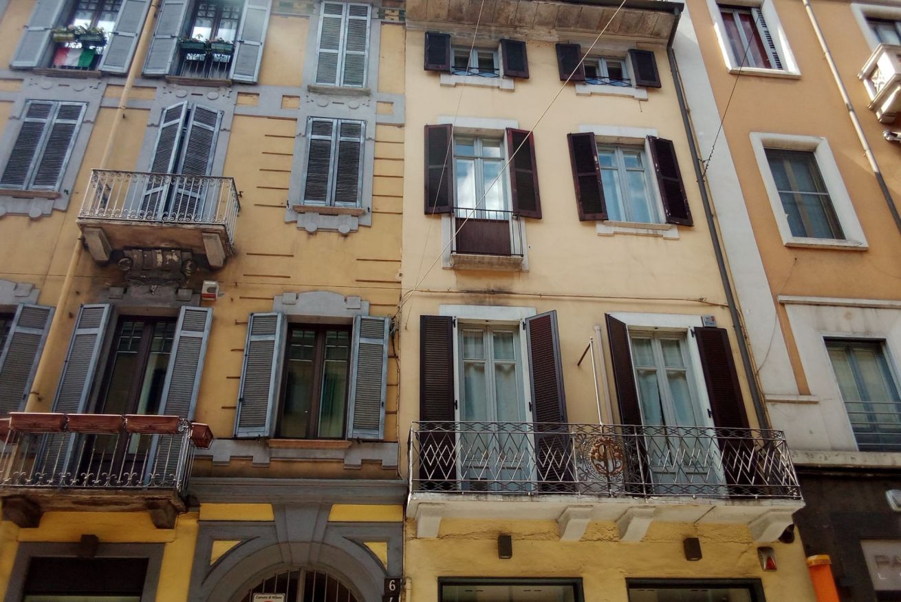 Un edificio de varios pisos con balcones, ventanas con contraventanas y una puerta a la vista.