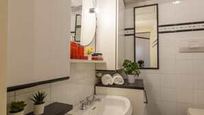 Une salle de bain avec un lavabo blanc, un miroir, un porte-serviettes et une plante en pot.