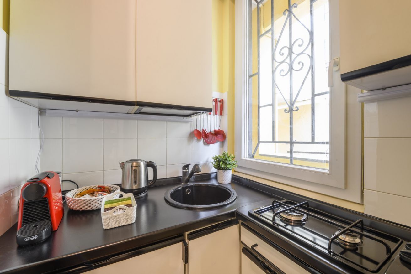 Een keuken met een gasfornuis, spoelbak, waterkoker en een raam met decoratieve ijzeren spijlen.