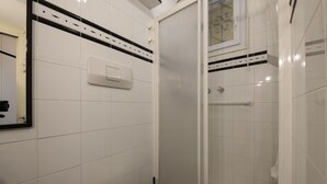 Un bagno con piastrelle bianche, un water, una doccia con porta in vetro e un asciugatore per le mani.