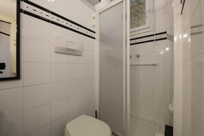 Un baño con azulejos blancos, un inodoro, una ducha con puerta de cristal y un secador de manos.