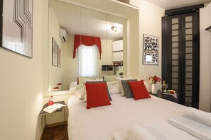 Habitación de hotel con una cama grande, una mesita de noche con lámpara, un espejo y un armario.