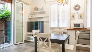 Une cuisine moderne avec des meubles blancs, une table à manger et des chaises. On y trouve également un téléviseur, un four à micro-ondes et un petit réfrigérateur.