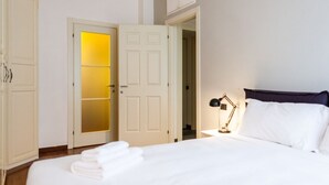 Une chambre d’hôtel comprenant un lit, une table de chevet, une lampe, une porte avec un panneau en verre dépoli et une armoire.