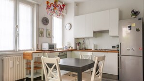 Une cuisine moderne avec des meubles blancs, un plan de travail en bois, une table à manger avec des chaises, un réfrigérateur et un lustre décoratif.