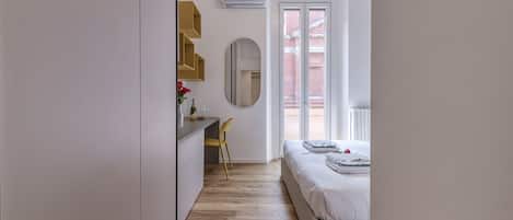 A bedroom with a bed, a desk, a chair, and a window.