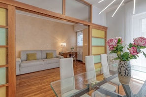 A modern living room with a sofa, a glass dining table, and a vase with flowers. - Stromboli, 22 – Elegante appartamento (Milano)