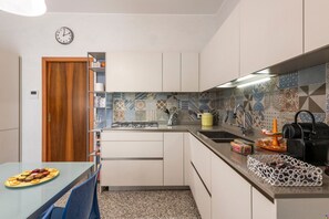 A compact kitchen with a wooden door, a clock, a tiled backsplash, and a dining area with a table set for two.