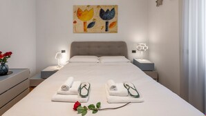 A neatly made bed with towels and slippers, a bedside lamp, a vase with flowers, and a wall art piece. - Stromboli, 22 – Elegante appartamento (Milano)