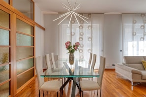 A modern dining area with a glass table, white chairs, a vase with flowers, and a contemporary light fixture. - Stromboli, 22 – Elegante appartamento (Milano)