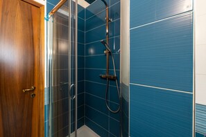 A bathroom with blue tiles, a glass shower enclosure, and a wooden door.