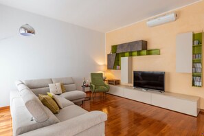 A modern living room with a sofa, a green armchair, a flat-screen TV, a lamp, and a bookshelf.