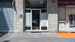 A building with a closed shutter on the left, a glass door entrance with a car inside, and a restaurant sign on the right. - Stromboli, 22 – Elegante appartamento (Milano)