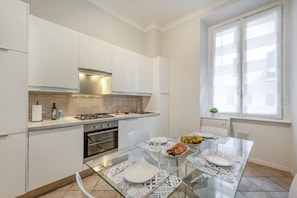Una cocina moderna con armarios blancos, una mesa de comedor de vidrio y una ventana con persianas.