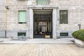 A stone building with a metal gate, a green window, and a small door. - Venini 14 - Tra Centrale e Buenos Aires (Milano)