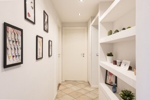 A hallway with framed artwork on the walls, a white door at the end, and shelves with decorative items. - Venini 14 - Tra Centrale e Buenos Aires (Milano)