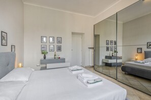 Un dormitorio moderno con un espejo grande, toallas ordenadamente dobladas, una mesita de noche con lámpara y cuadros enmarcados en la pared.