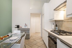 Una cocina compacta con estufa a gas, cafetera y comedor con mesa de vidrio y sillas.