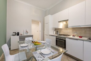 A compact kitchen with white cabinets, a gas stove, and a dining area with a glass table and chairs. - Venini 14 - Tra Centrale e Buenos Aires (Milano)