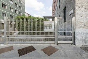 A gated entrance with a metal gate, a security booth, and a building with a stone facade. - Venini 14 - Tra Centrale e Buenos Aires (Milano)