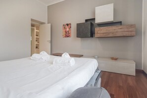 Una habitación de hotel con una cama, una mesita de noche, un banco, un estante en la pared y una puerta que da a un armario.