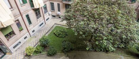 Un patio con un árbol grande, un pequeño jardín y suelo de baldosas.