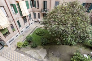 Un patio con un árbol grande, un pequeño jardín y suelo de baldosas.