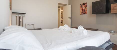 Una habitación de hotel con cama, una silla, un radiador, un cuadro y un televisor en la pared.