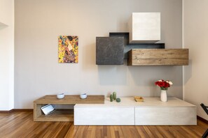 A modern living room with a wooden floor, a white console table, a painting, a marble block, and a vase with flowers. - Venini 14 - Tra Centrale e Buenos Aires (Milano)