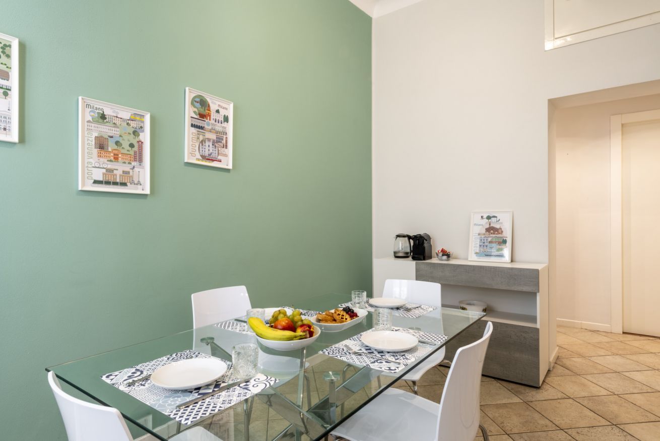 A dining area with a glass table, white chairs, and a bowl of fruit.