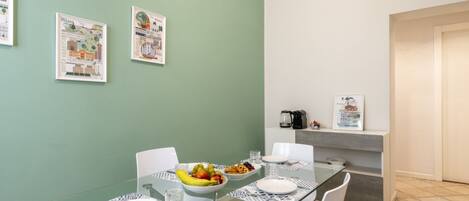 A dining area with a glass table, white chairs, and a bowl of fruit.