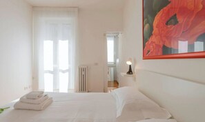 Een hotelkamer met een bed, een radiator, een deur en een schilderij aan de muur.