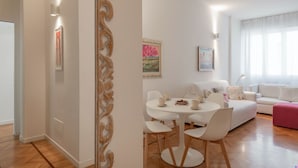 A modern living room with a white sofa, a round dining table with chairs, and a pink ottoman. - Verona 12, Porta Romana district (Milano)