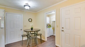A dining area with a round table and four stools, a ceiling light fixture, and a door leading to a kitchen. - Bring the Whole Alumni Crew Close to Ole Miss (Oxford)