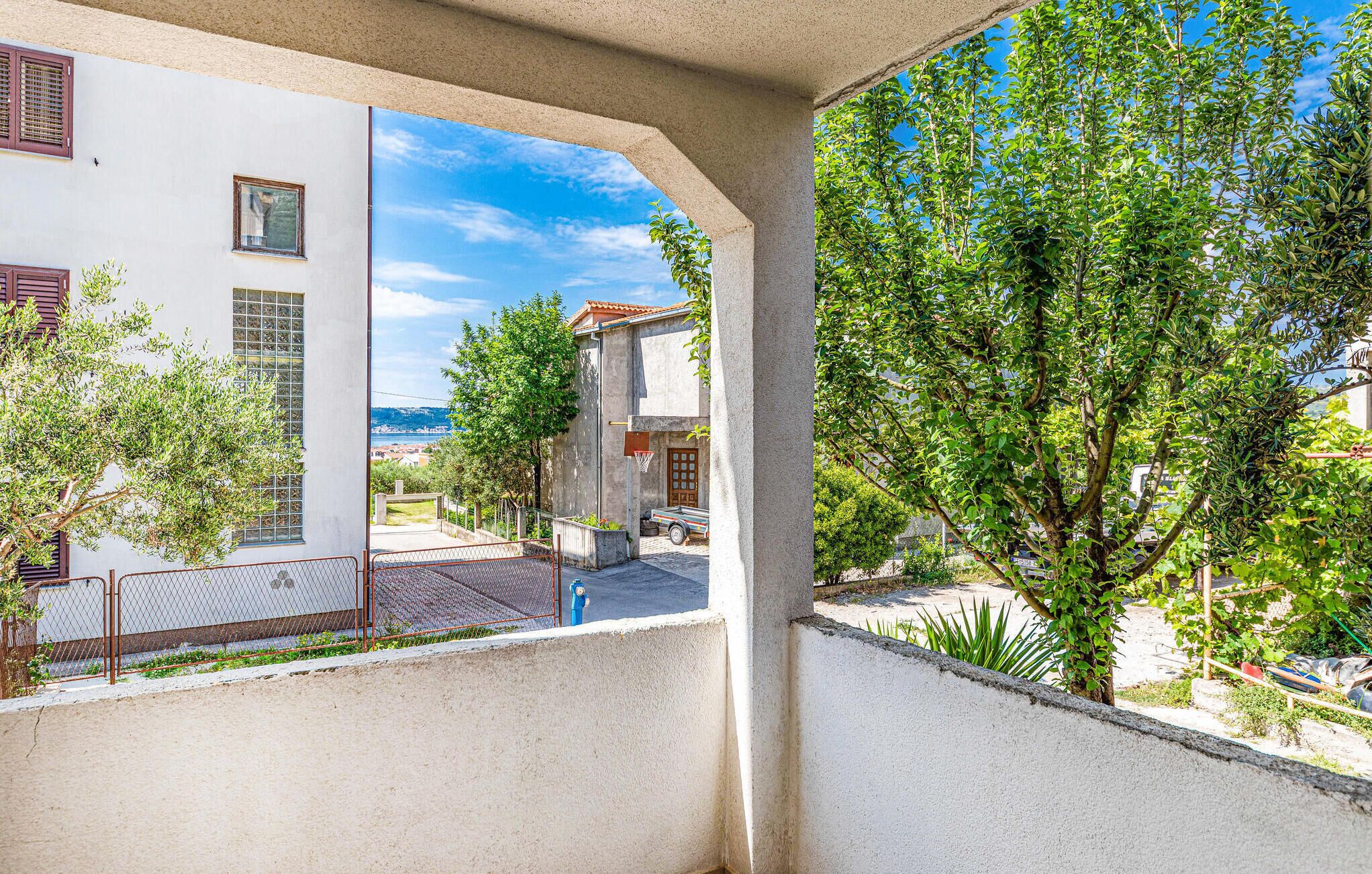 A balcony with a view of a white building, a tree, and a clear blue sky.