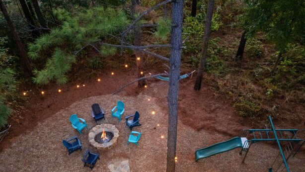 A fire pit surrounded by chairs in a forested area with a slide.