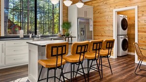 Una cocina moderna con paredes de madera, un ventanal grande, taburetes de bar y lavadora integrada.