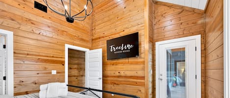 A wooden-paneled room with a bed, a television, and a sign for 'Teline Vacation Rentals'.