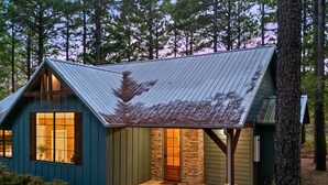 A small, single-story cabin with a sloped metal roof, a stone foundation, and a large window on the front.