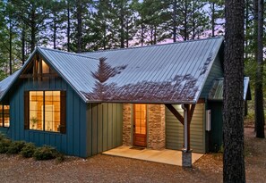 A small, single-story cabin with a sloped metal roof, a stone foundation, and a large window on the front.