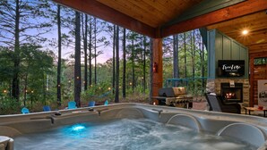 A hot tub with a view of a forest, a television, and a grill area.