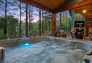 A hot tub with a view of a forest, a television, and a grill area.