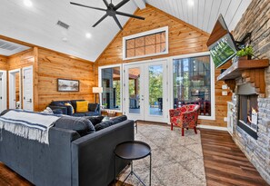 A modern log cabin interior with a living room, a fireplace, and a large window overlooking the outdoors. - Secluded Hot Tub Retreat for Families and Friends (Broken Bow)