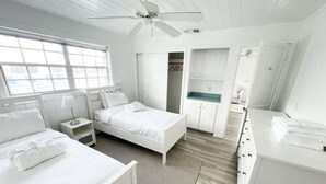 A white-themed bedroom with a bed, bedside tables, a wardrobe, and a bathroom with a sink and mirror.