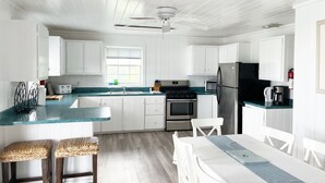 A modern kitchen with white cabinets, a teal countertop, a central island with stools, a dining table, and a ceiling fan.