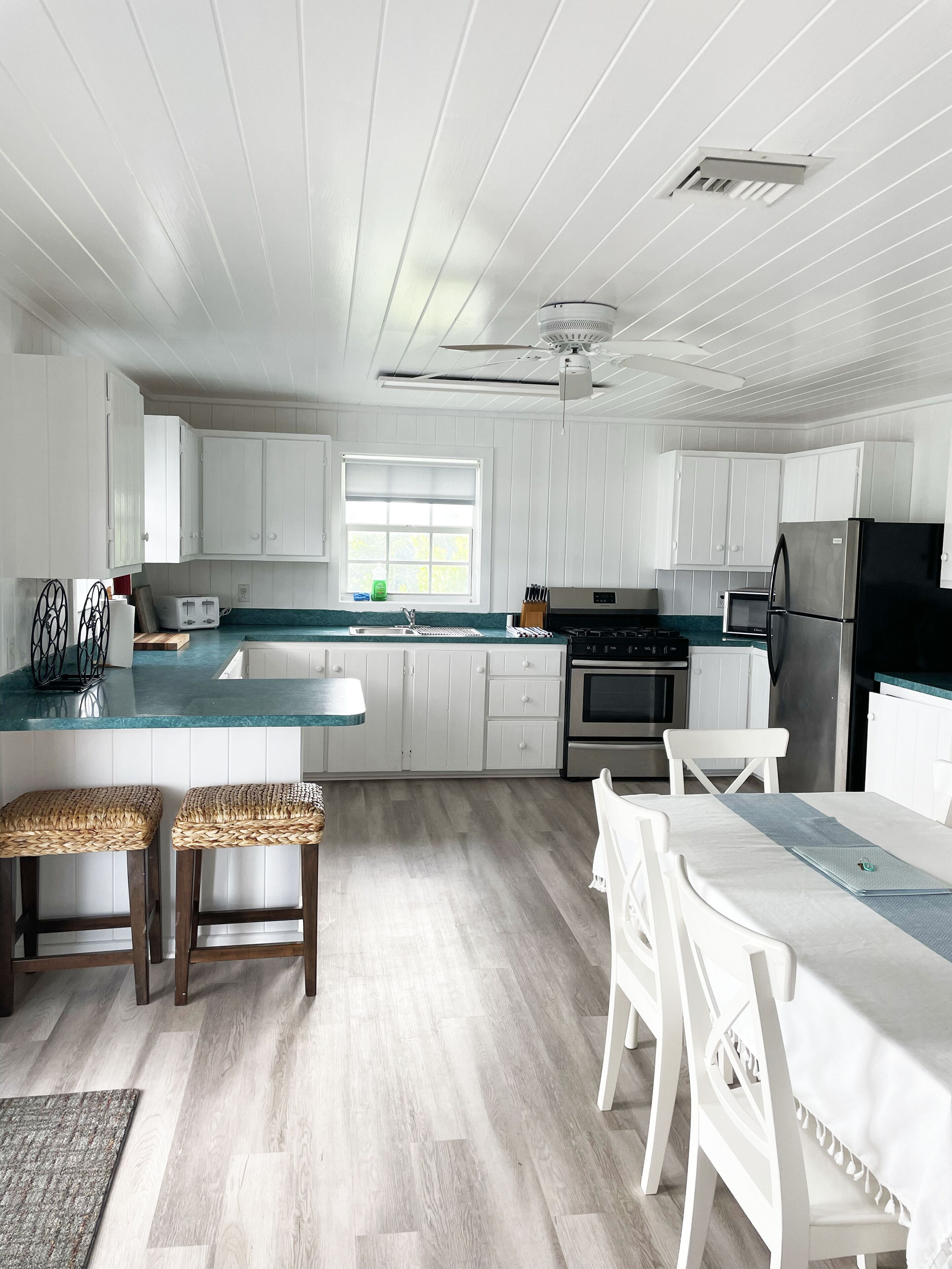 Une cuisine moderne avec des meubles blancs, un îlot central, un coin repas avec des chaises blanches et une grande fenêtre qui laisse entrer la lumière naturelle.
