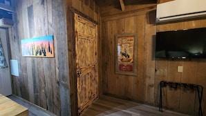 Un interno rustico in legno, con una porta in legno, un quadro incorniciato, una televisione a parete e una panca in legno.